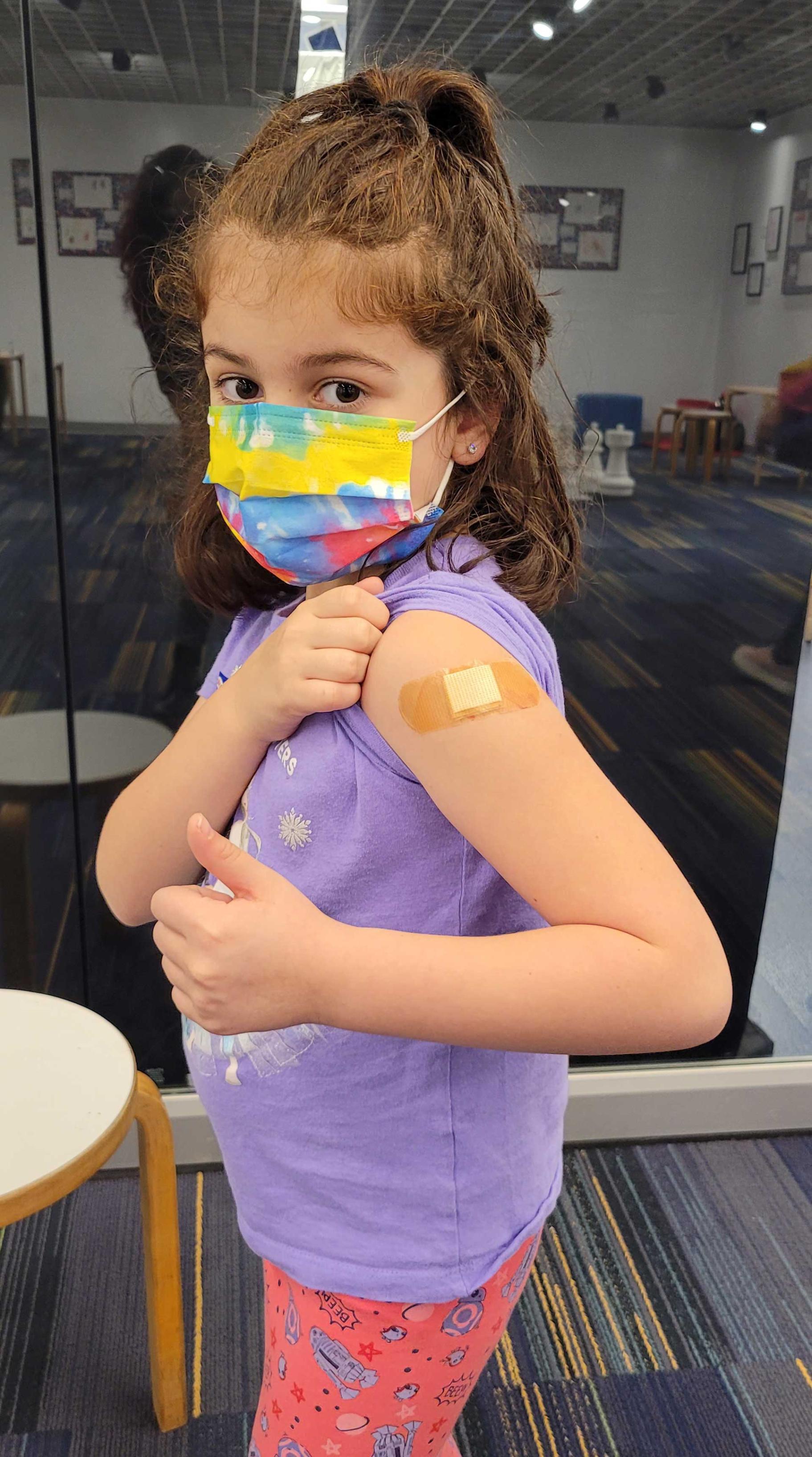 a young girl shows the band-aid on her arm where she just received a vaccination